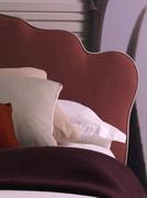 Detail of headboard upholstered in burgundy fabric with contrasting profile