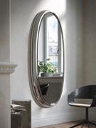 Example of Genesi mirror in its smoky grey full-length version positioned in a living or reading area context
