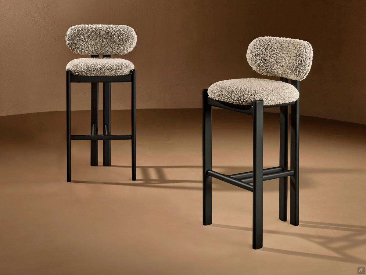 Mailea upholstered bar stool with a low back, with a painted metal or solid ash wood structure; seat covered in fabric, velvet or leather