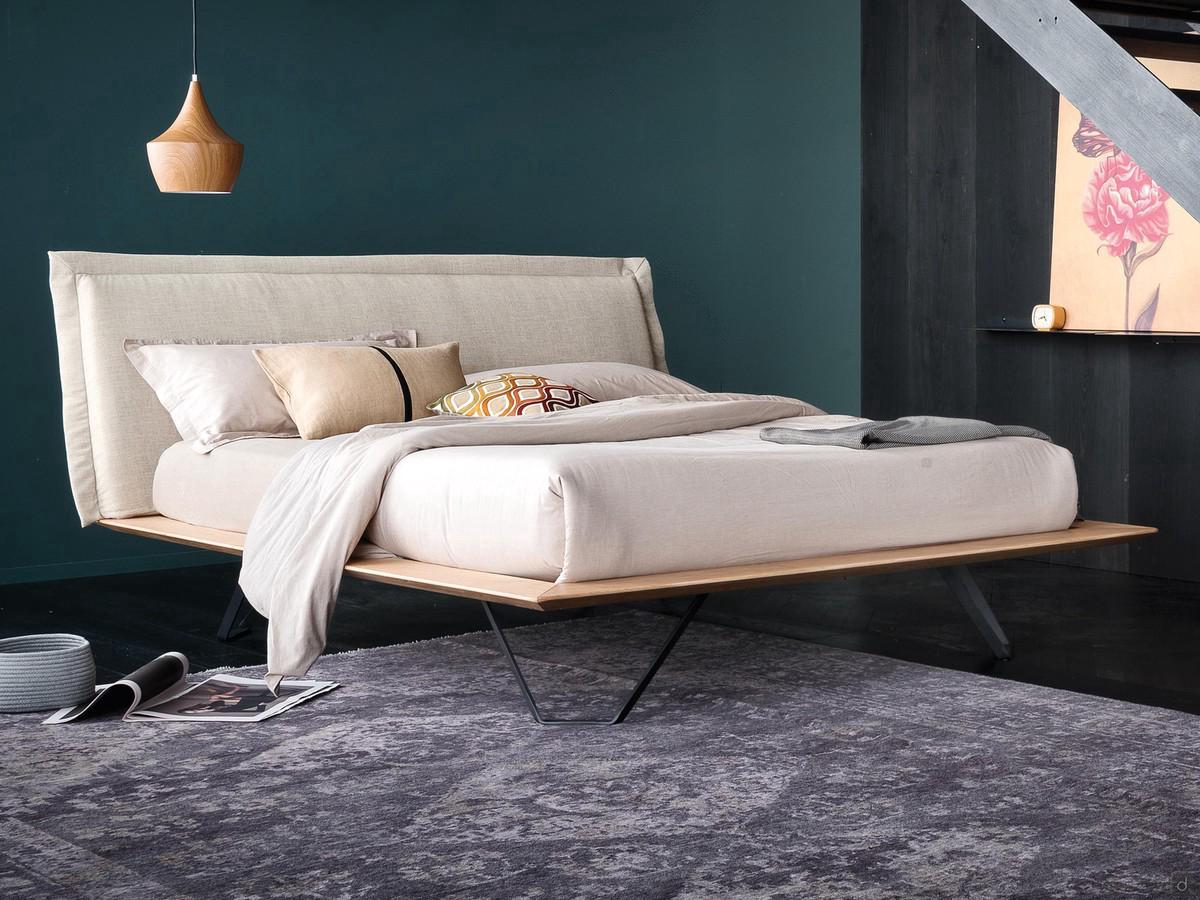 Lit Miguel en bois avec de hauts pieds en métal, ici dans la version avec tête de lit rembourrée et recouverte de tissu