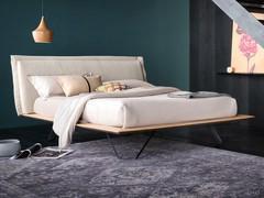 Lit Miguel en bois avec de hauts pieds en métal, ici dans la version avec tête de lit rembourrée et recouverte de tissu