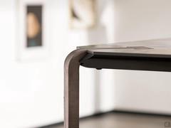 Vista frontale di dettaglio dell'incastro tra le gambe in metallo curvato verniciato od ossidato e il piano in ceramica. Si nota il supporto della lastra in mdf colore nero