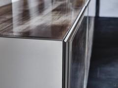Particolare dell'anta con profilo metallico goffrato titanio e lastra in cristallo applicata. Si apprezzano anche il top rivestito in vetro in tinta alle ante e il fianco il legno laccato opaco bianco