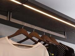 Dettaglio delle barre led in fresata nella parte inferiore dei ripiani e dei tubi appendiabiti in metallo verniciato moka shine