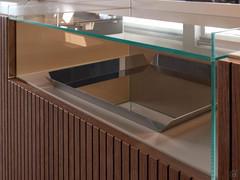 Dettaglio del vano a giorno con piano superiore e fianchi in vetro trasparente, inserito in un porta Tv con frontali in groove wood Biscotto e struttura e top laccato opaco Sabbia