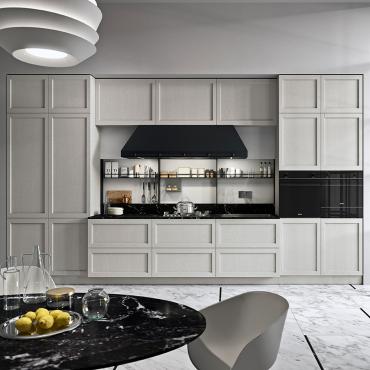 Cucina lineare con frigo, forno e microonde integrati nelle colonne laterali. Piano di lavoro centrale con cappa stile industriale.