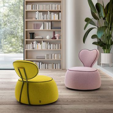 Petit Fauteuil sans accoudoir pour chambre à coucher. Alice a une base en forme de pouf et un dossier ovale ou en forme de coeur. Disponible en tissu, similicuir ou velours