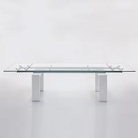 Table à rallonges en verre Brooklyn avec structure laquée blanche, rail en aluminium anodisé et plateau en verre transparent - vue du côté plus long
