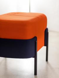 Dettaglio del pouf Just con seduta in tessuto arancio, struttura rivestita a contrasto in tessuto nero e gambe in metallo nero opaco