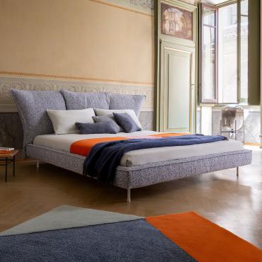 Madame C is an upholstered bed with slim feet and 3 big cushions that compose the headboard by Bonaldo