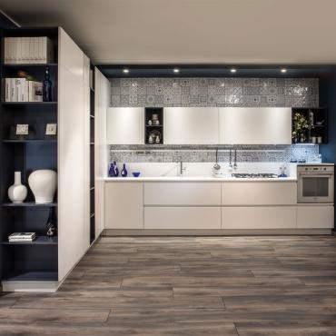 Matt white kitchen without handles, L-shaped with columns, top with integrated sink, glass hob and vasistas wall units