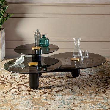 Tavolino con tre piani d'appoggio Cosmo caratterizzato da: struttura in frassino nero, piani in vetro fumè trasparente e bottone centrale in metallo laccato oro opaco.