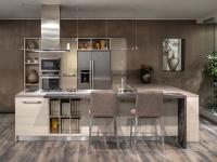 L-shaped kitchen with island, without wall units and integrated snack countertop; equipped by oven columns, pantry and double-door fridge.
