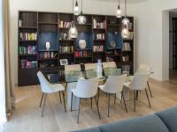 Dining area equipped with glass and stone table, velvet and metal chairs, veneered and lacquered bookcase