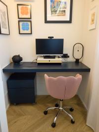 Angolo studio home office con mensolone sospeso blu, sedia da ufficio rosa, cassettiera blu con ruote.