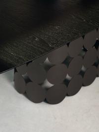 Detail der Maserung der Platte aus schwarzer Esche und des Sockels, der aus der Verbindung runder Metallelemente entsteht