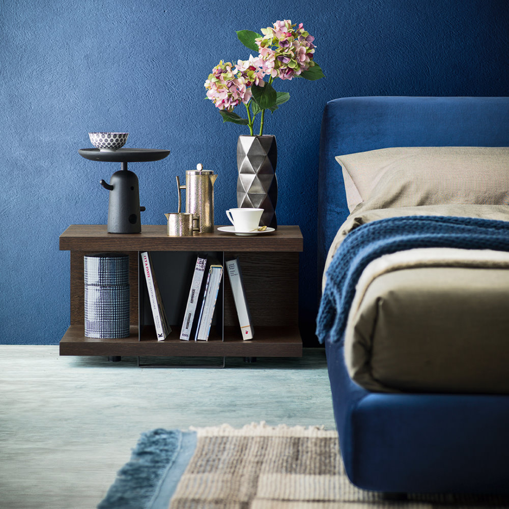 Vista frontale di un comodino in legno scuro accanto a un letto tessile blu