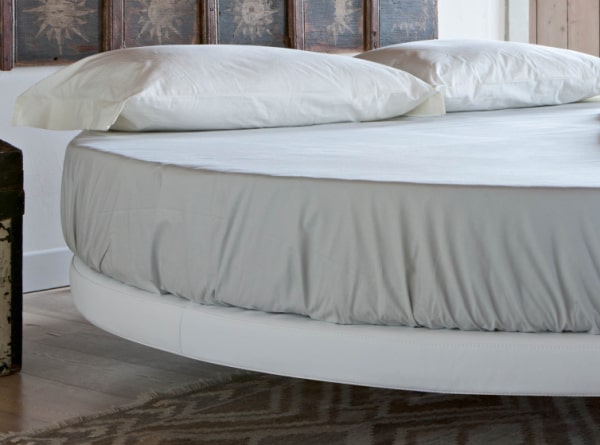 Dettaglio di un letto rotondo con base in pelle bianca sollevata da terra